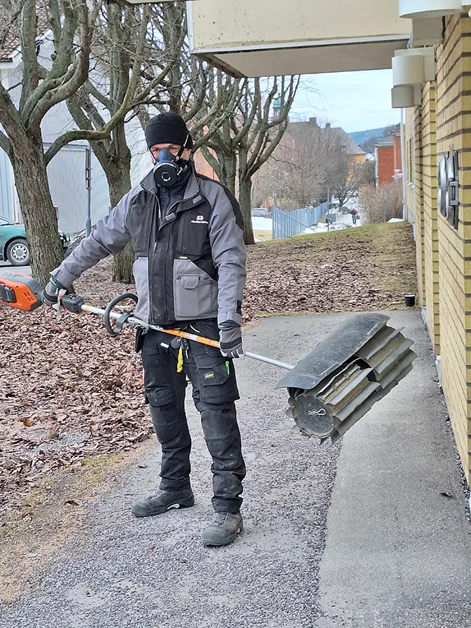 Fastighetsskötare med soputrustning och andningsmask